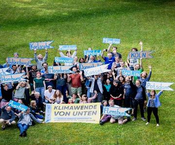 Das Bild zeigt das Team von Klimawende von unten auf einer Wiese, wie sie Plakate hochhalten.