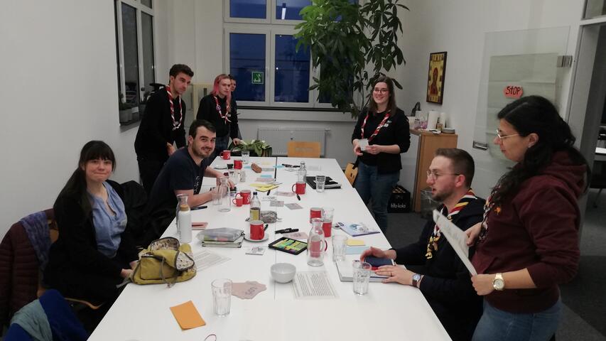 7 Menschen sitzen an einem langen Tisch und tauschen sich aus.