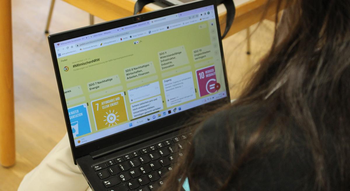 Eine Person sitzt mit dem Laptop auf dem Schoß auf einem Stuhl und schaut sich das Padlet mit den Forderungen an.