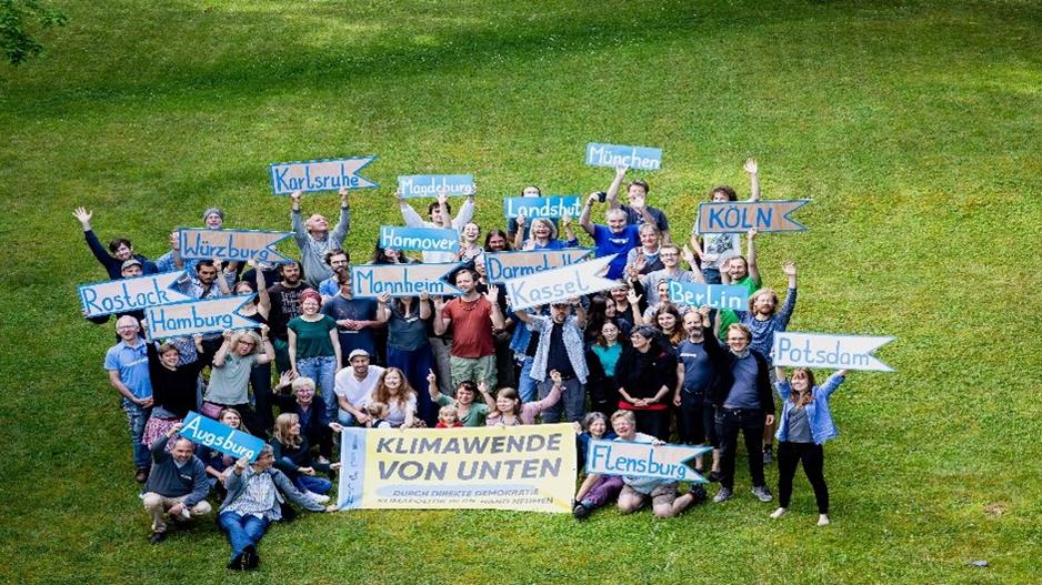 Das Bild zeigt das Team von Klimawende von unten auf einer Wiese, wie sie Plakate hochhalten.