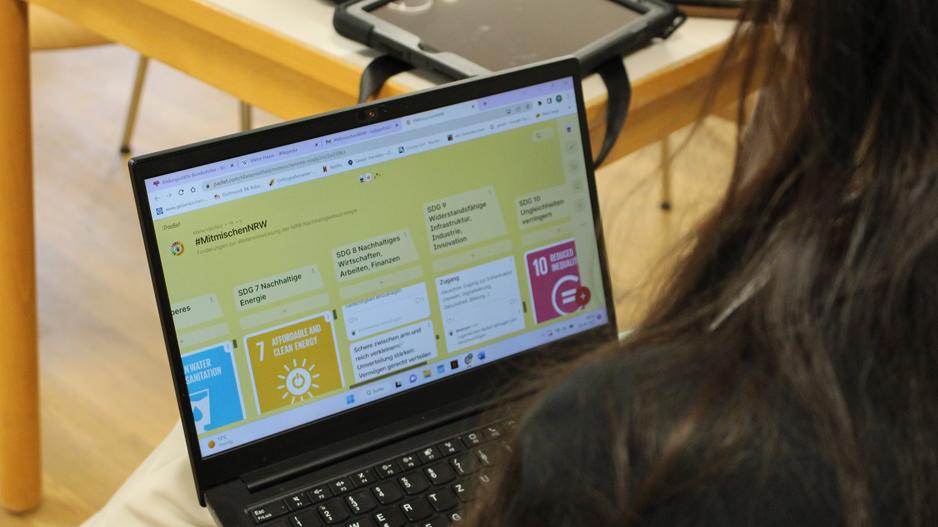 Eine Person sitzt mit dem Laptop auf dem Schoß auf einem Stuhl und schaut sich das Padlet mit den Forderungen an.