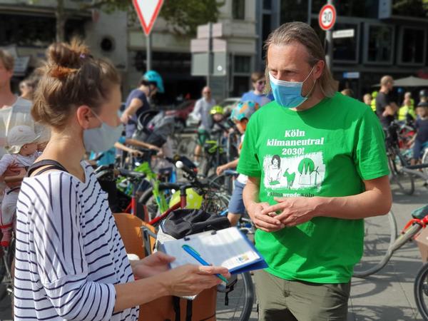 Auf dem Bild sieht man ein Mitglied der Initiative Klimawende von unten beim Unterschriftensammeln in Köln.