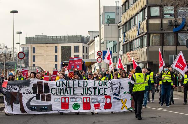 Das Bild zeigt eine Gruppe Demonstrierende, die den ersten Block bei der großen Klimademo in Bonn im März 2023 bilden. Diese halten ein Banner mit dem Spruch "United for Climate Justice". Ebenfalls in der ersten Reihe befinden sich Mitarbeitende von der Gewerkschaft verdi.