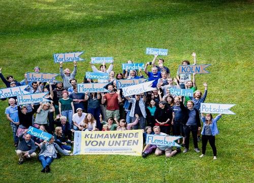 Das Bild zeigt das Team von Klimawende von unten auf einer Wiese, wie sie Plakate hochhalten.